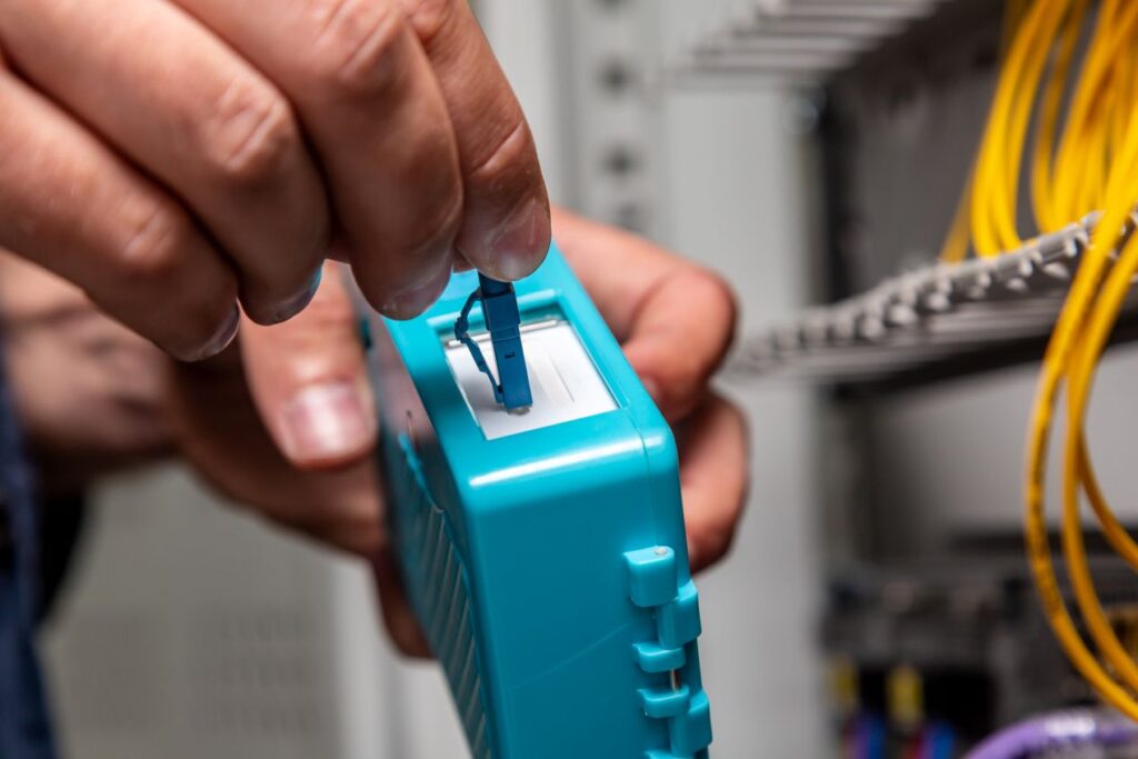 Hände verwenden LWL Werkzeug zur Steckerreinigung direkt am Patchpanel mit Glasfaserkabeln